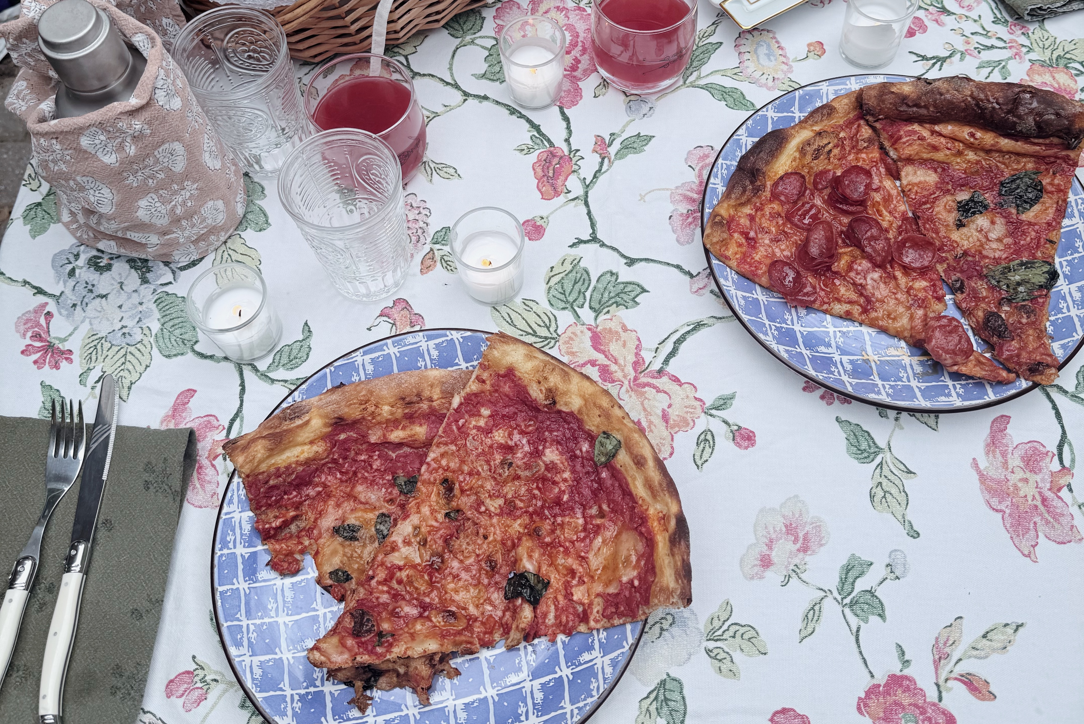 Weeknight dinner set outdoors with pizza, candles, floral tablecloth, and blue patterned plates